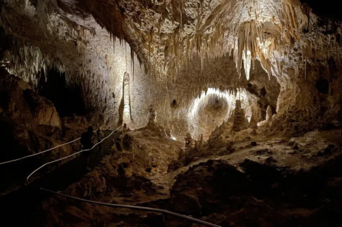 A dimly lit cave interior featuring stalactites and stalagmites, with a pathway winding through the rocky terrain.