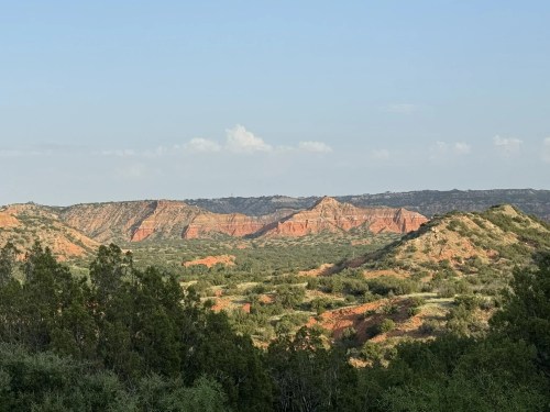A scenic view of layered red rock formations and green vegetation under a clear blue sky.