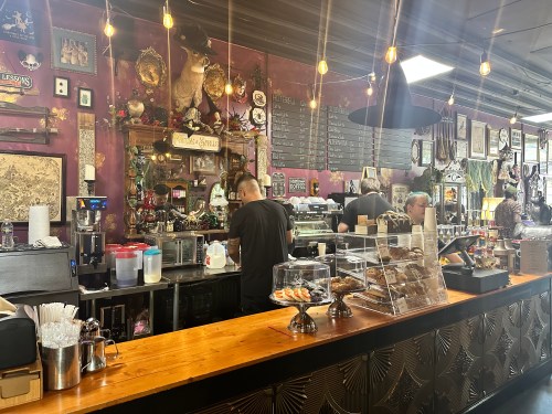 A cozy café interior with a wooden counter, baristas preparing drinks, and vintage decor on the walls.