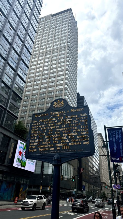 A historical marker for Reading Terminal & Market in Philadelphia, with a tall building in the background.
