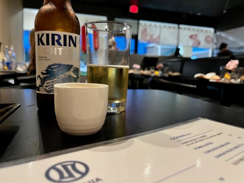 A table setting featuring a Kirin beer bottle, a glass of beer, a small sake cup, and a menu in a restaurant.