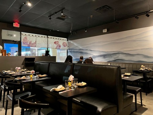 Interior of a modern restaurant with black booths, a mural of mountains, and tables set with flowers and utensils.