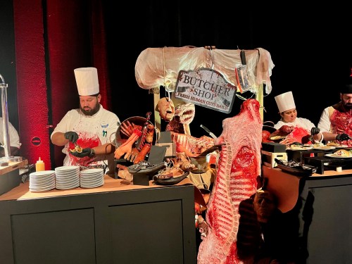 Chefs at a butcher shop display, preparing meats with various cuts and garnishes in a festive setting.