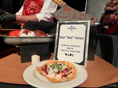 A heart-shaped tostada topped with red beet tartar, hummus, vegan feta, and watercress on a crispy tortilla.