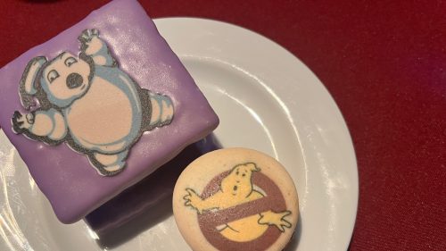 A purple dessert with a cartoon polar bear and a cookie featuring the Ghostbusters logo on a white plate.