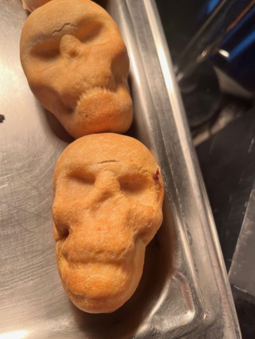 Two baked goods shaped like skulls, resting on a metal tray.