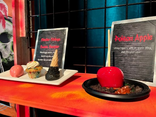 A display of themed desserts: a cupcake, a cone, and a red candy apple on a black plate, with descriptive signs.