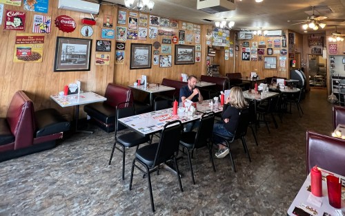 A cozy diner interior with wooden walls, vintage decor, and two patrons sitting at a table.