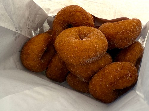 A bag filled with freshly made, golden-brown donuts coated in sugar.