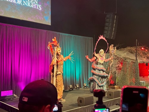 Two elaborately dressed performers on stage during a Halloween event, with colorful lighting and a festive backdrop.
