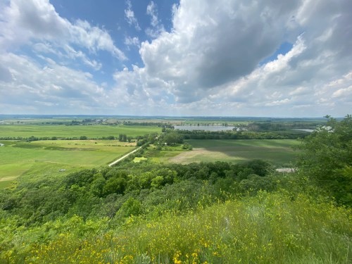 A scenic view of lush green fields and a river under a partly cloudy sky.