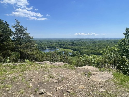 A scenic view from a rocky overlook, showcasing a lush green landscape and a winding river under a clear blue sky.