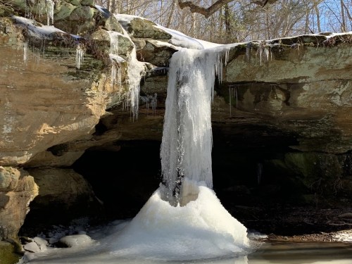 A frozen waterfall cascading over rocky cliffs, surrounded by ice and snow in a serene natural setting.