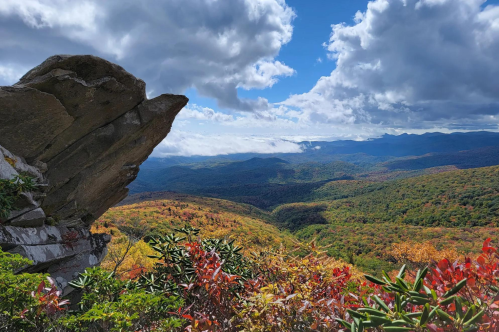 A panoramic view of colorful autumn foliage in the mountains under a partly cloudy sky.