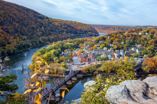 A scenic view of a river town surrounded by autumn foliage and hills, with a bridge crossing the river.