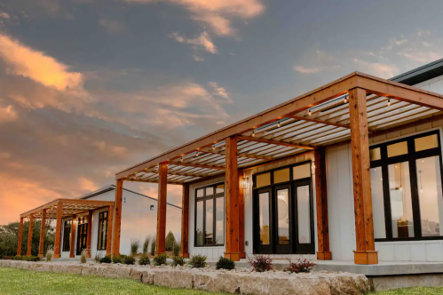 Modern building with wooden pergolas, large windows, and a scenic sunset sky in the background.