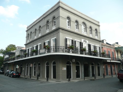 Historic gray building with arched windows and balconies, located at a street corner in a vibrant urban setting.