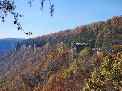 A scenic view of a colorful autumn landscape with rocky cliffs and trees in vibrant fall foliage under a clear blue sky.