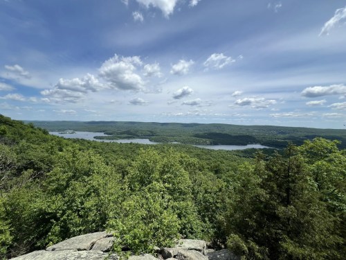 A scenic view of a lush green landscape with a lake, rolling hills, and a blue sky dotted with clouds.