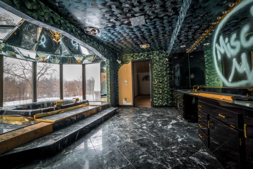 Luxurious bathroom with dark marble floors, green patterned walls, a large tub, and large windows overlooking a snowy landscape.
