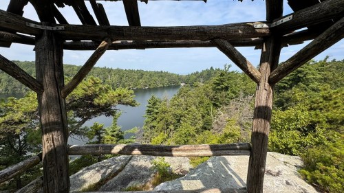 View of a serene lake surrounded by trees, framed by a rustic wooden structure.