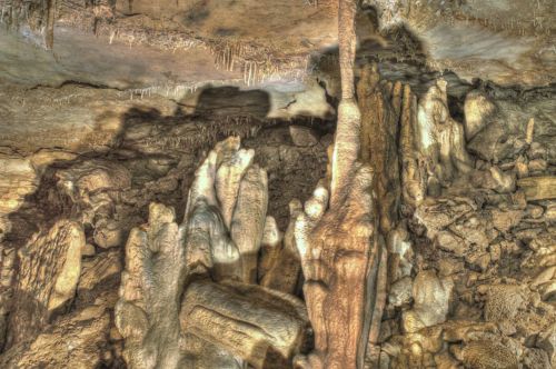 Stalactites and stalagmites in a dimly lit cave, showcasing intricate rock formations and textures.