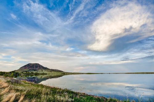 A serene landscape featuring a mountain reflected in a calm lake under a blue sky with scattered clouds.