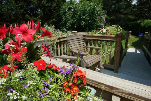 A wooden deck surrounded by vibrant flowers in a lush garden, featuring a cozy seating area.