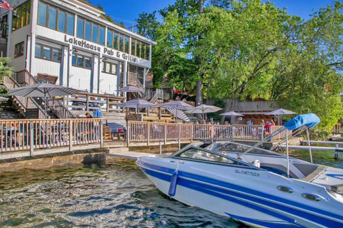 A boat approaches the LakeHouse Pub & Grille, surrounded by trees and outdoor seating by the water.