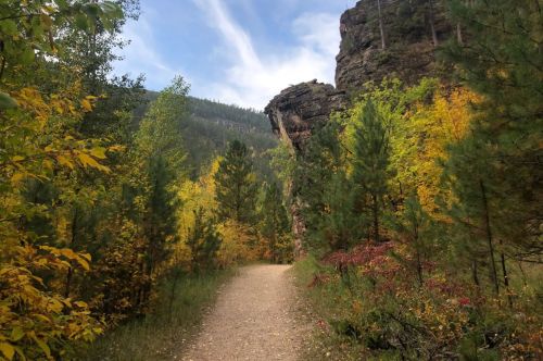 A scenic trail surrounded by vibrant autumn foliage and rocky cliffs under a blue sky.