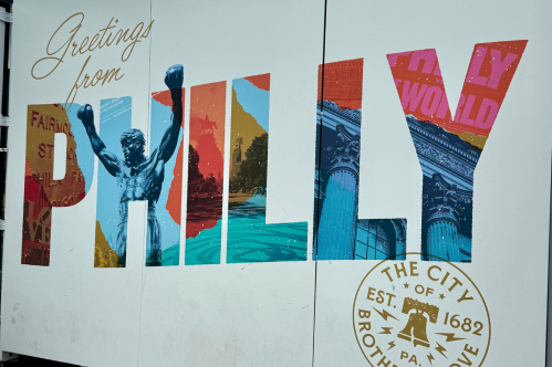 Colorful mural reading "Greetings from Philly" with iconic Philadelphia imagery and the city seal.