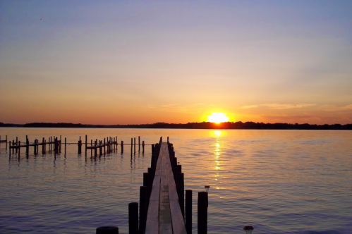 A serene sunset over a calm lake, viewed from a wooden pier extending into the water.