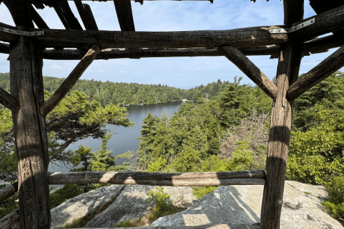 View of a serene lake surrounded by trees, framed by a rustic wooden structure.