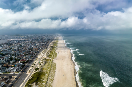 Aerial view of a sandy beach with waves, coastal town, and cloudy sky in the background.