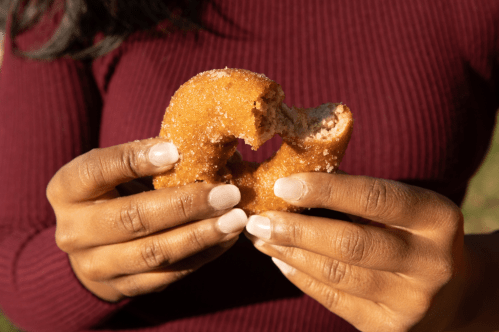 A person holds a partially eaten donut, showcasing its sugary coating and soft texture.