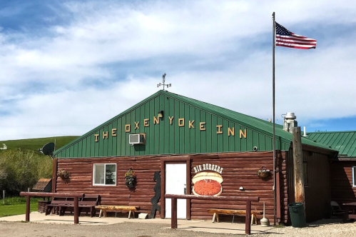 A rustic building with a green roof and wooden exterior, featuring a sign that reads "The Oxen Yoke Inn" and an American flag.