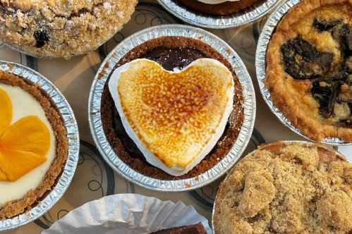 A variety of mini pies, featuring a heart-shaped pie with a toasted top in the center, surrounded by other desserts.