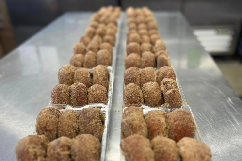 Rows of freshly made doughnut holes coated in cinnamon sugar, arranged neatly on a stainless steel surface.