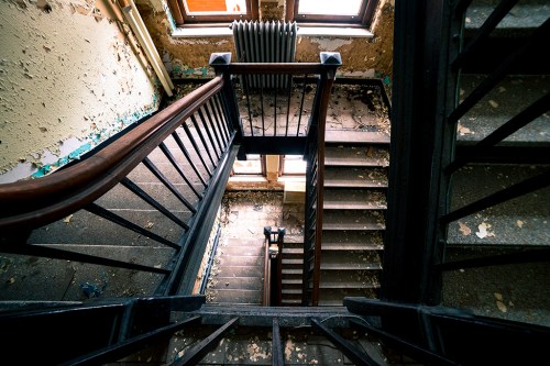 A view from above of a worn staircase with peeling paint and a vintage radiator, illuminated by natural light.