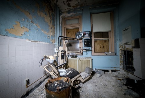 Abandoned room with peeling blue paint, scattered debris, and old appliances in disrepair.