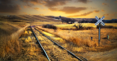 Rustic railroad tracks cross a golden field under a dramatic sunset sky in North Dakota.