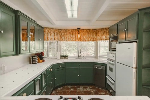 Cozy kitchen with green cabinets, white countertops, and a sunny window with floral curtains.