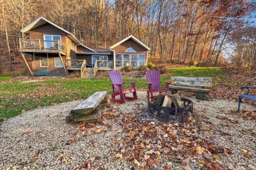 A cozy cabin surrounded by autumn foliage, featuring a fire pit and seating area in a serene outdoor setting.