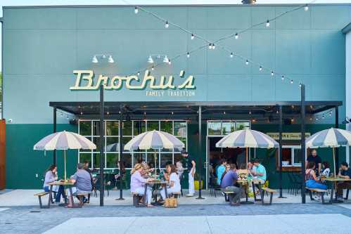 Outdoor dining scene at Brochu's, featuring patrons at tables under umbrellas, with string lights overhead.