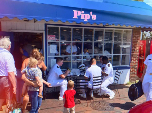 A busy restaurant scene with naval personnel dining outside, while families and children wait nearby.