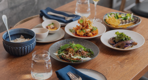 A wooden table set with various dishes, including rice, seafood, and vegetables, alongside a glass of water and napkins.