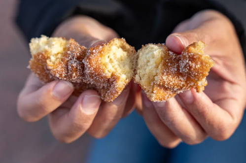 A person holds a split, sugary donut, revealing its soft, fluffy interior.