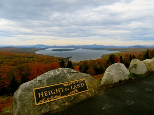 A scenic view from Height of Land, showcasing a lake surrounded by autumn foliage and cloudy skies.