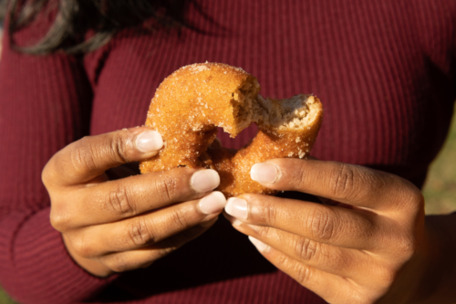 A person holds a partially eaten donut with a sugary coating, showcasing their hands and the treat.