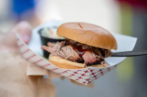A close-up of a pulled pork sandwich on a bun, served with a side of coleslaw in a small container.